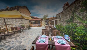 An outdoor dining area with stone walls, wooden tables, and chairs. - Kadilar Pasazade Konagi Butik Otel (Odemis)