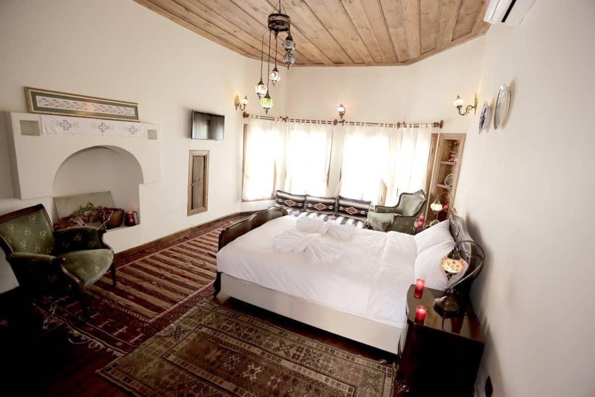 Une chambre à coucher de style traditionnel, dotée d’un grand lit, d’une cheminée, d’un lustre et d’un plafond en bois classique.
