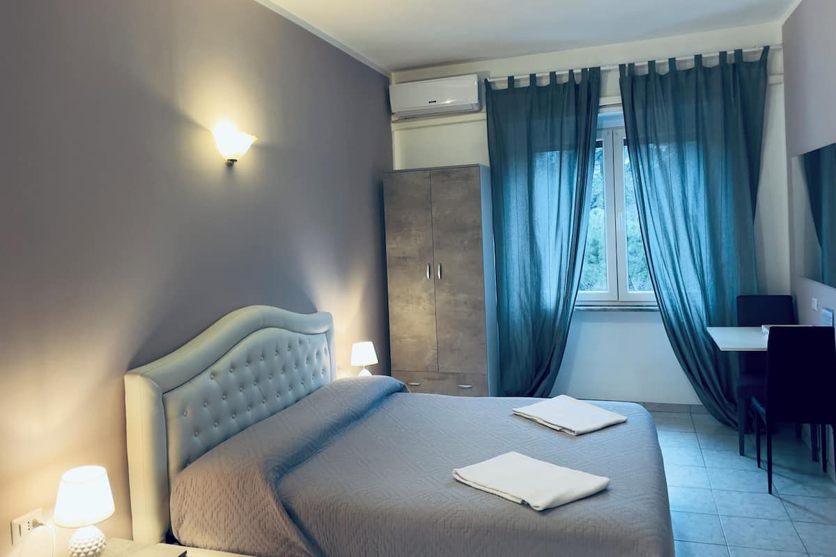 A modern bedroom with a large bed, a desk, and a wardrobe.