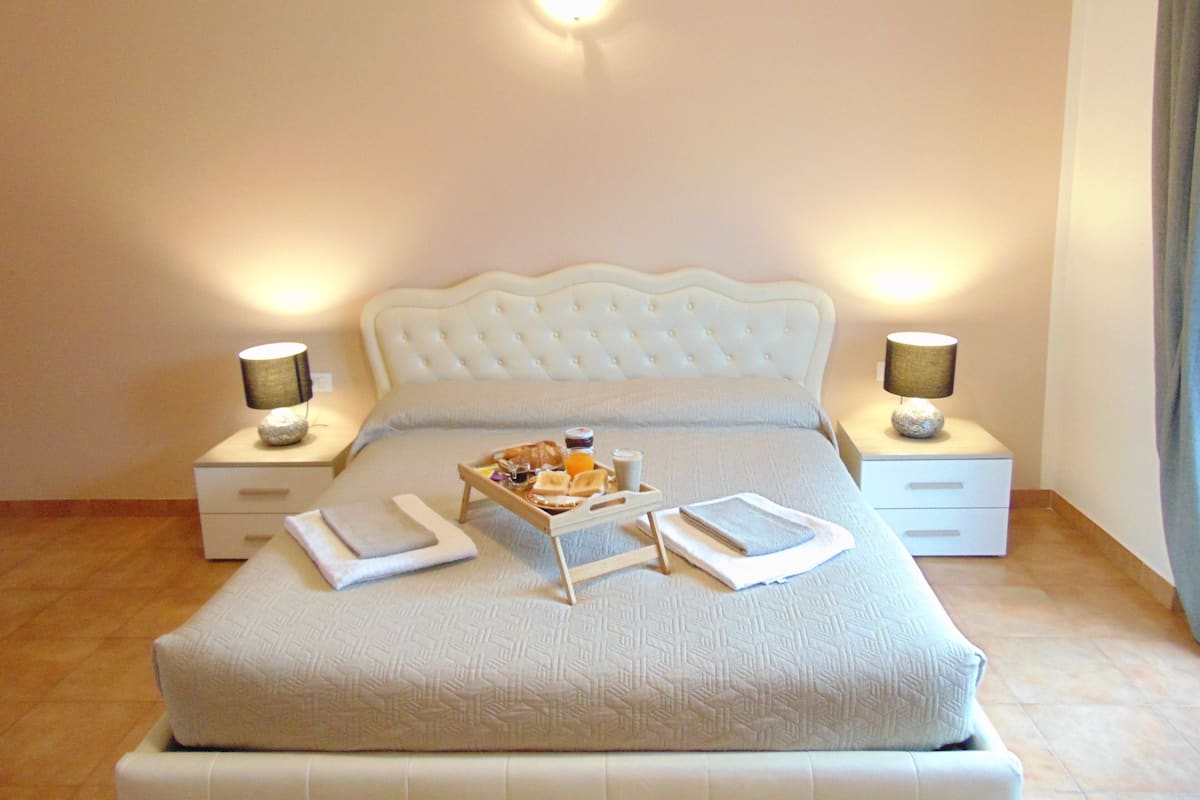 A neatly made bed with a tray of breakfast items, two bedside lamps, and a nightstand with a lamp.