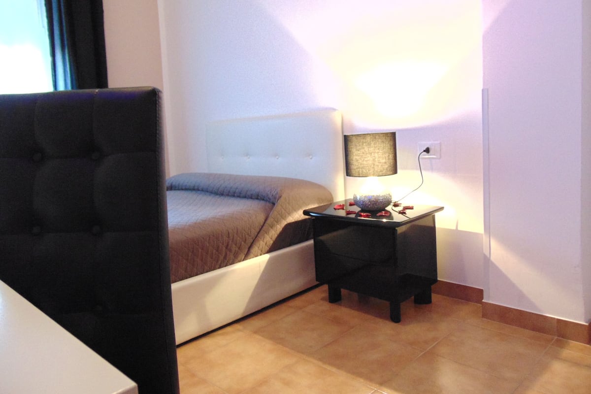A bedroom with a bed, a bedside table with a lamp, and a chair.
