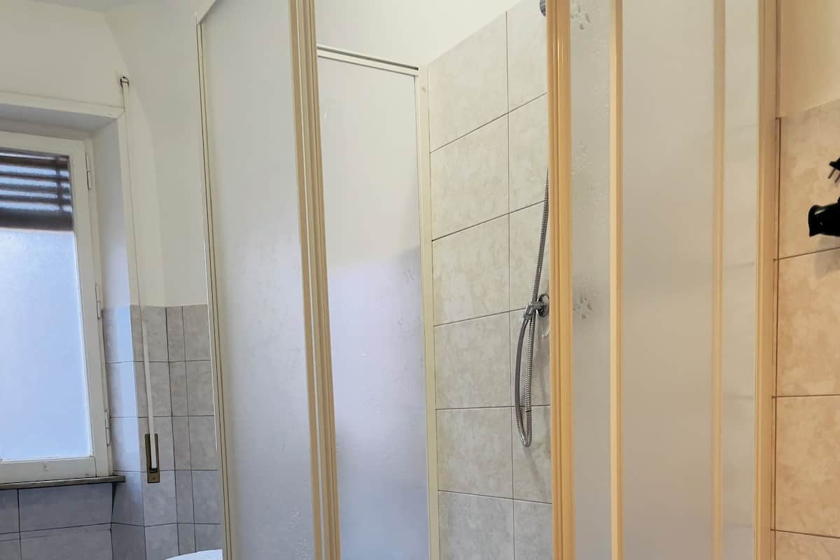 A modern bathroom with a glass-enclosed shower, a toilet, and a window.
