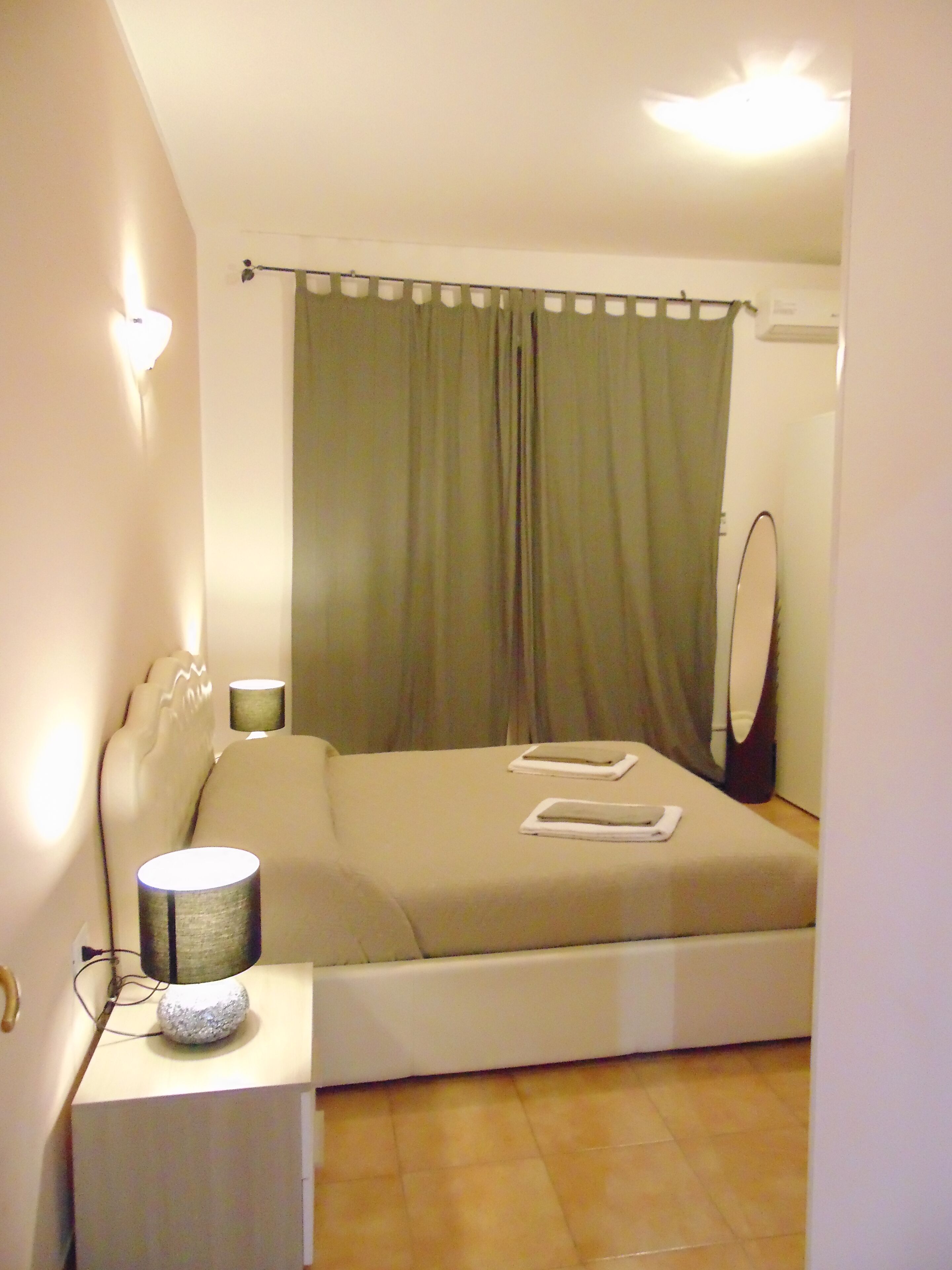 Un dormitorio con cama, lámparas de noche, un espejo y una cortina.