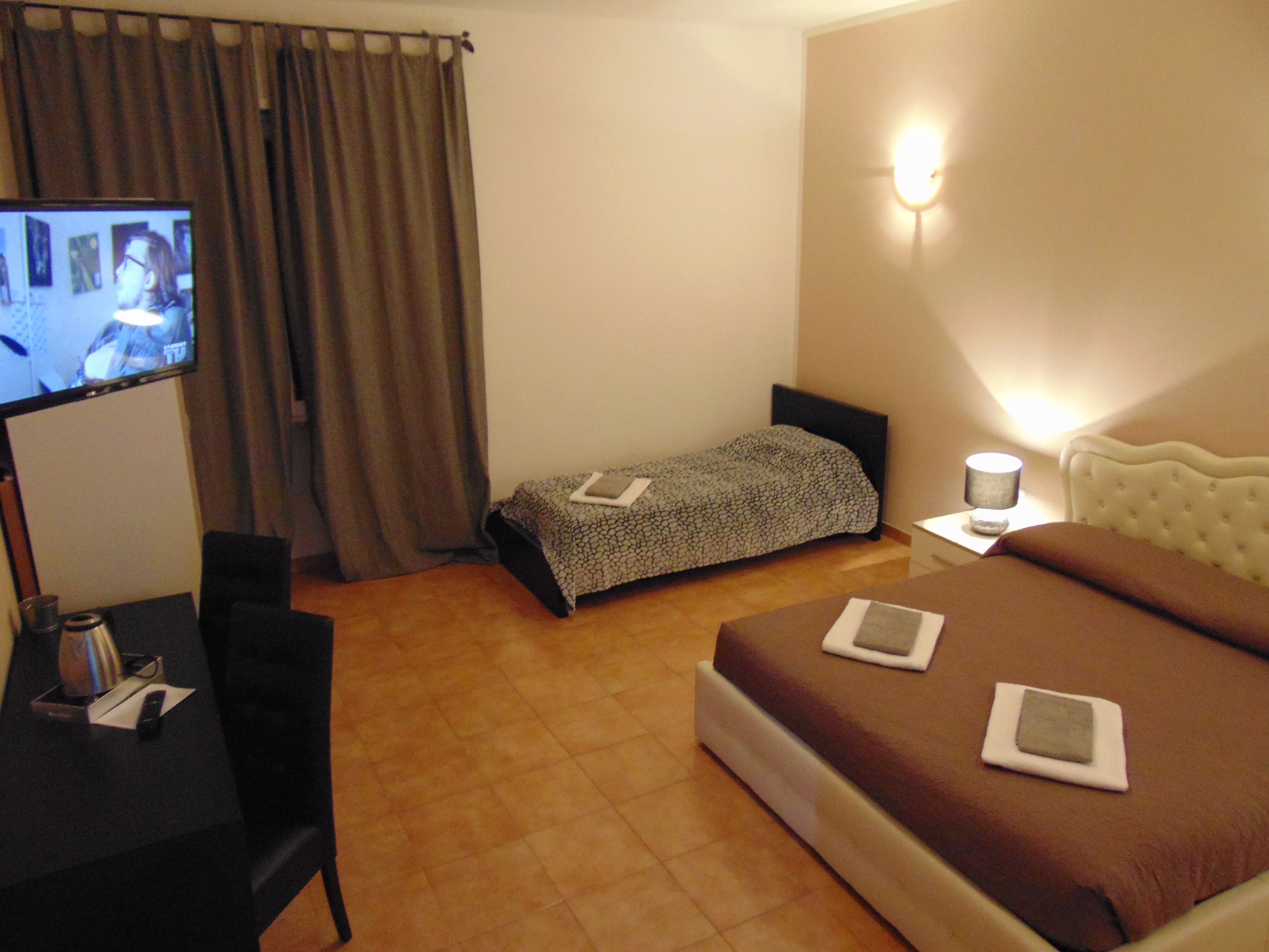 A hotel room with a bed, a desk with a chair, a television, and a bedside table with a lamp.