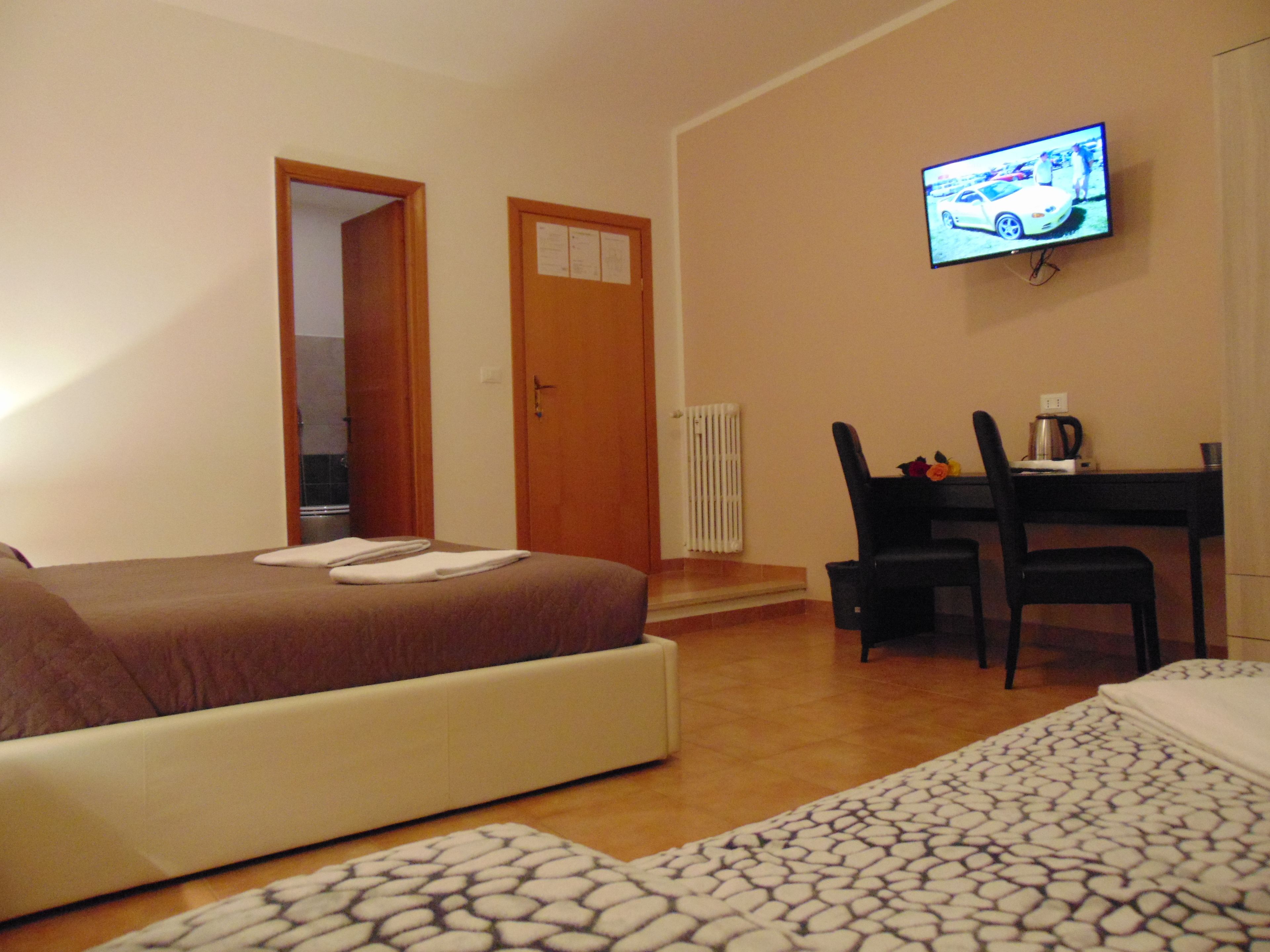 A hotel room with a bed, a desk, a chair, a television, and a radiator.