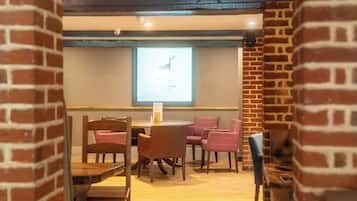 Un salón de conferencias con una pantalla de proyector mostrando una imagen de un ciervo, sillas de madera, una mesa y paredes de ladrillo.