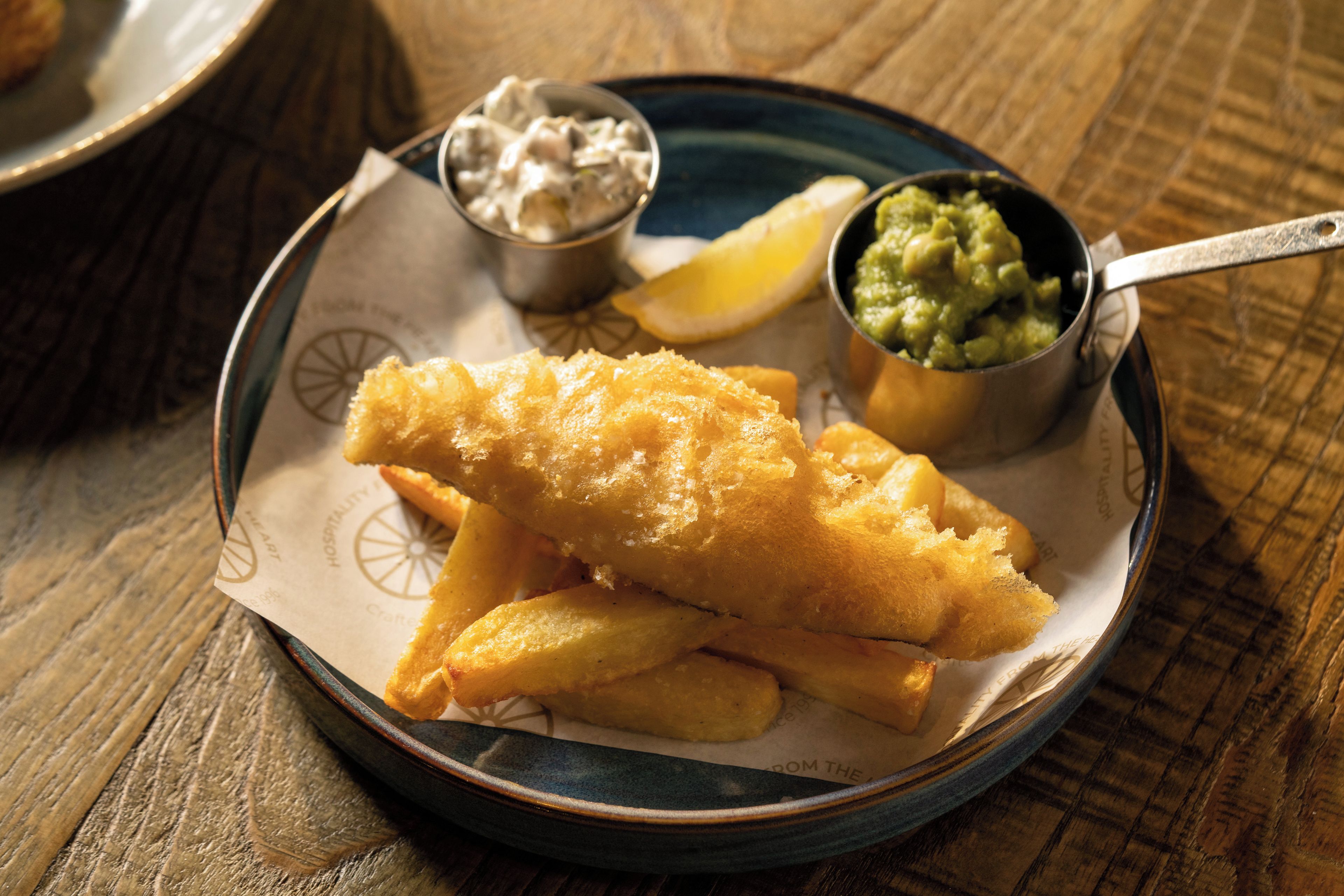 A plate with fish and chips, lemon wedge, tartar sauce, and mushy peas.