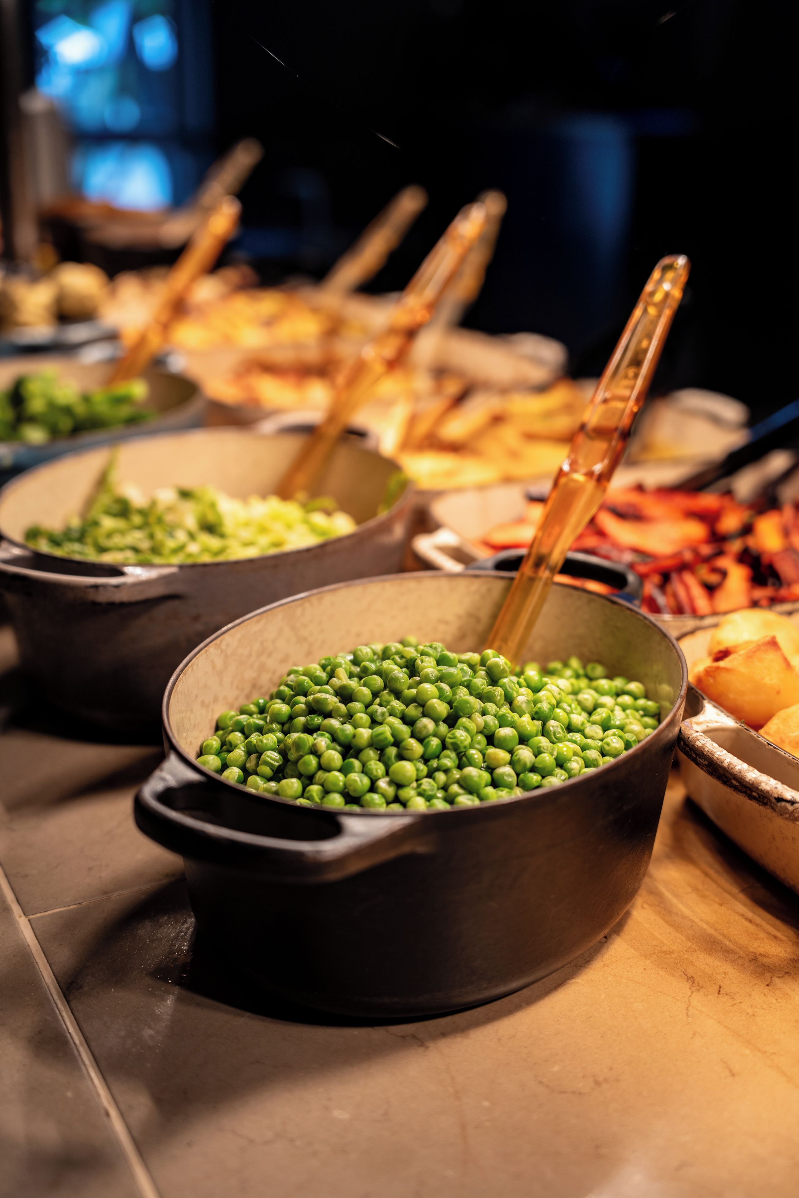 A buffet table with multiple bowls of food, including peas and other dishes.