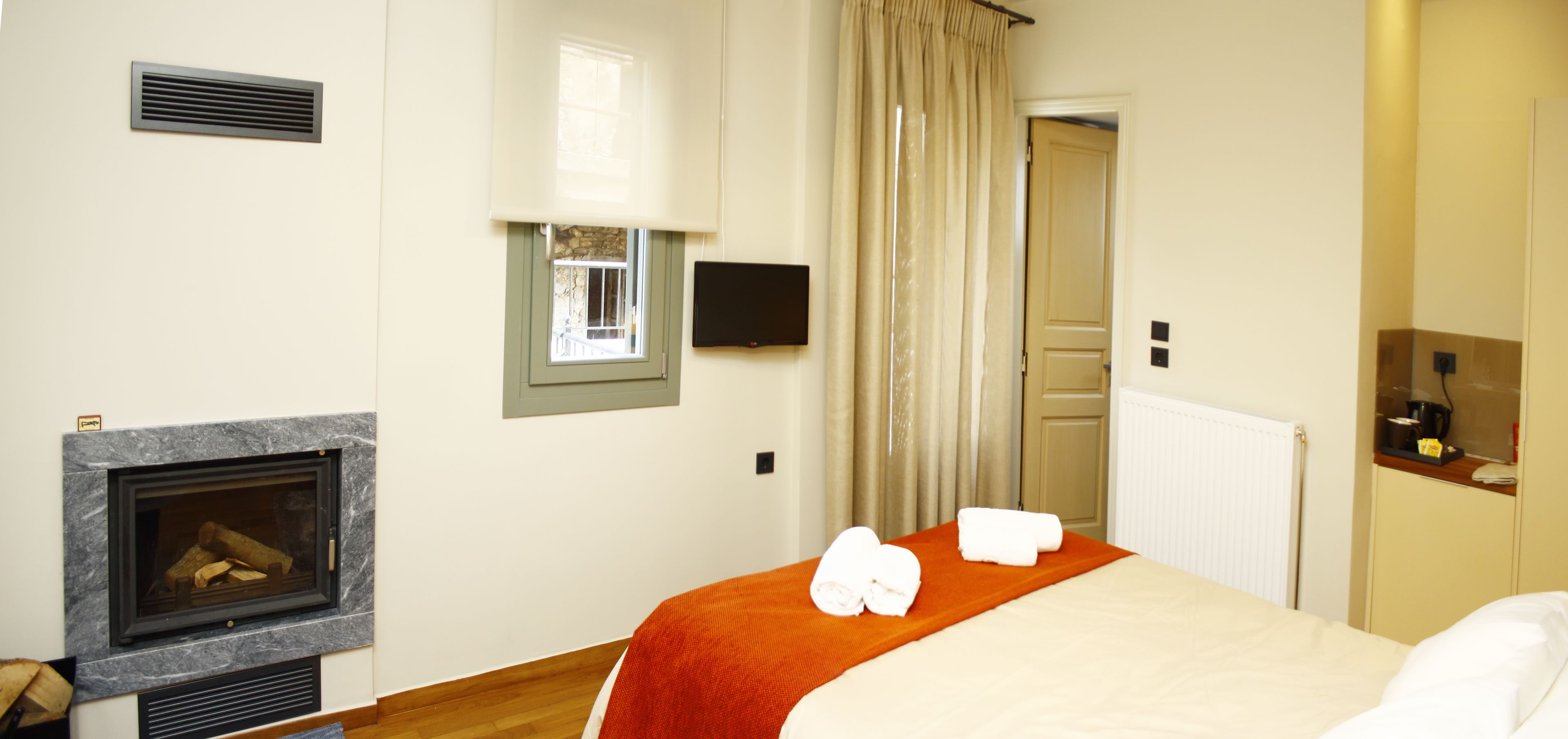 A hotel room with a fireplace, a bed with an orange blanket, and a window with curtains.