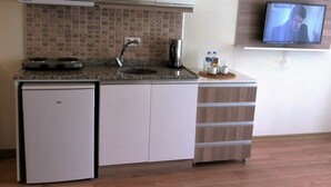Eine kompakte Küche mit einer Mikrowelle, einem kleinen Kühlschrank und einem Spülbecken. Ein Fernseher ist über dem Tresen an der Wand befestigt.