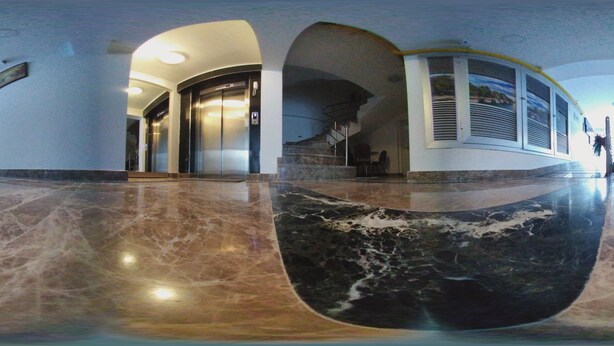 Eine Lobby mit poliertem Marmorboden, zwei Aufzügen und einer Treppe, die in eine obere Etage führt.