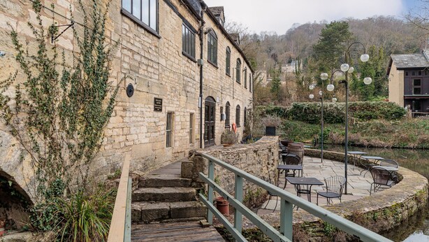 Ein Steinhaus mit einer Holztreppe, die zu einer Terrasse mit Sitzgelegenheiten im Freien führt.