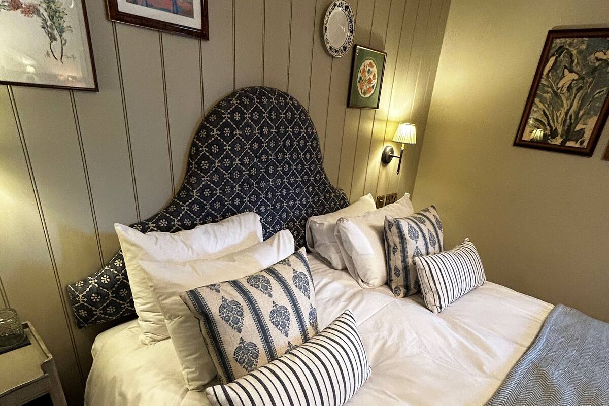 A neatly made bed with a patterned headboard, multiple pillows, and a striped throw.