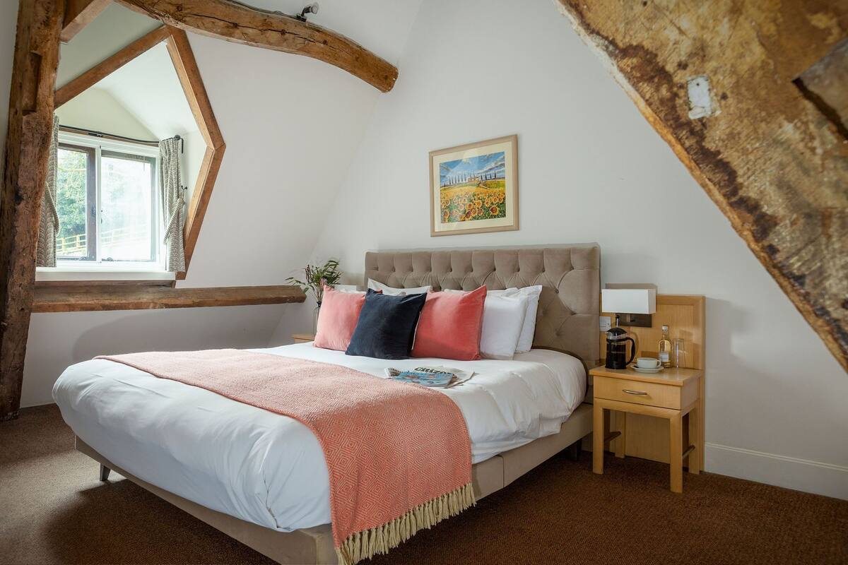 A bedroom with a large bed, a nightstand, a window, and a painting on the wall.