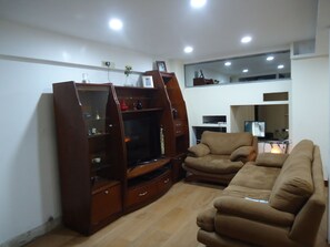 Una sala de estar con un sofá marrón, un mueble de madera para entretenimiento y un televisor.