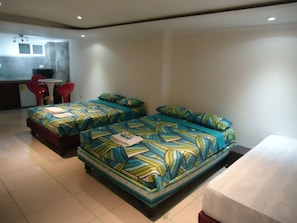 Habitación de hotel con dos camas, una kitchenette pequeña y una zona de comedor con sillas rojas.