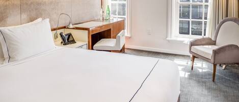 A hotel room with a large bed, a desk, a chair, and a window.
