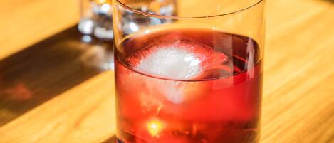 A glass of red beverage with ice cubes and a lemon slice garnish on a wooden table.