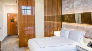 Hotelkamer met een groot bed, een houten garderobe, een nachtkastje met lamp en uitzicht op de stad door een raam.