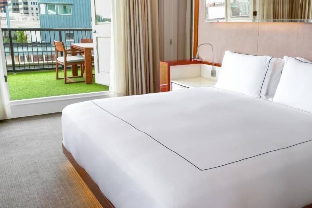 Een hotelkamer met een groot bed, een bureau, een stoel en uitzicht op een groen buitengebied.