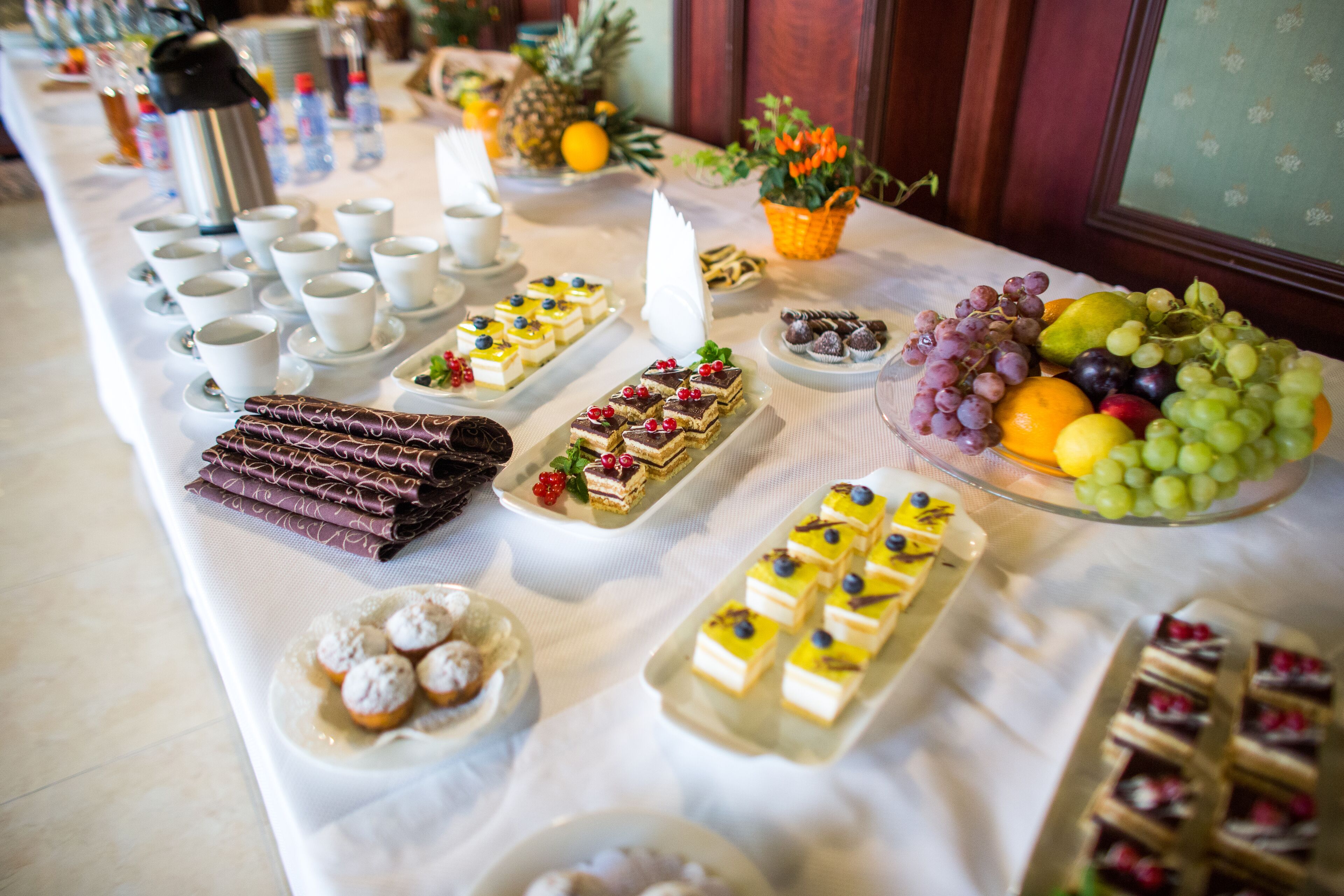 A buffet table with various desserts and fruits, including cakes, pastries, and a fruit basket.