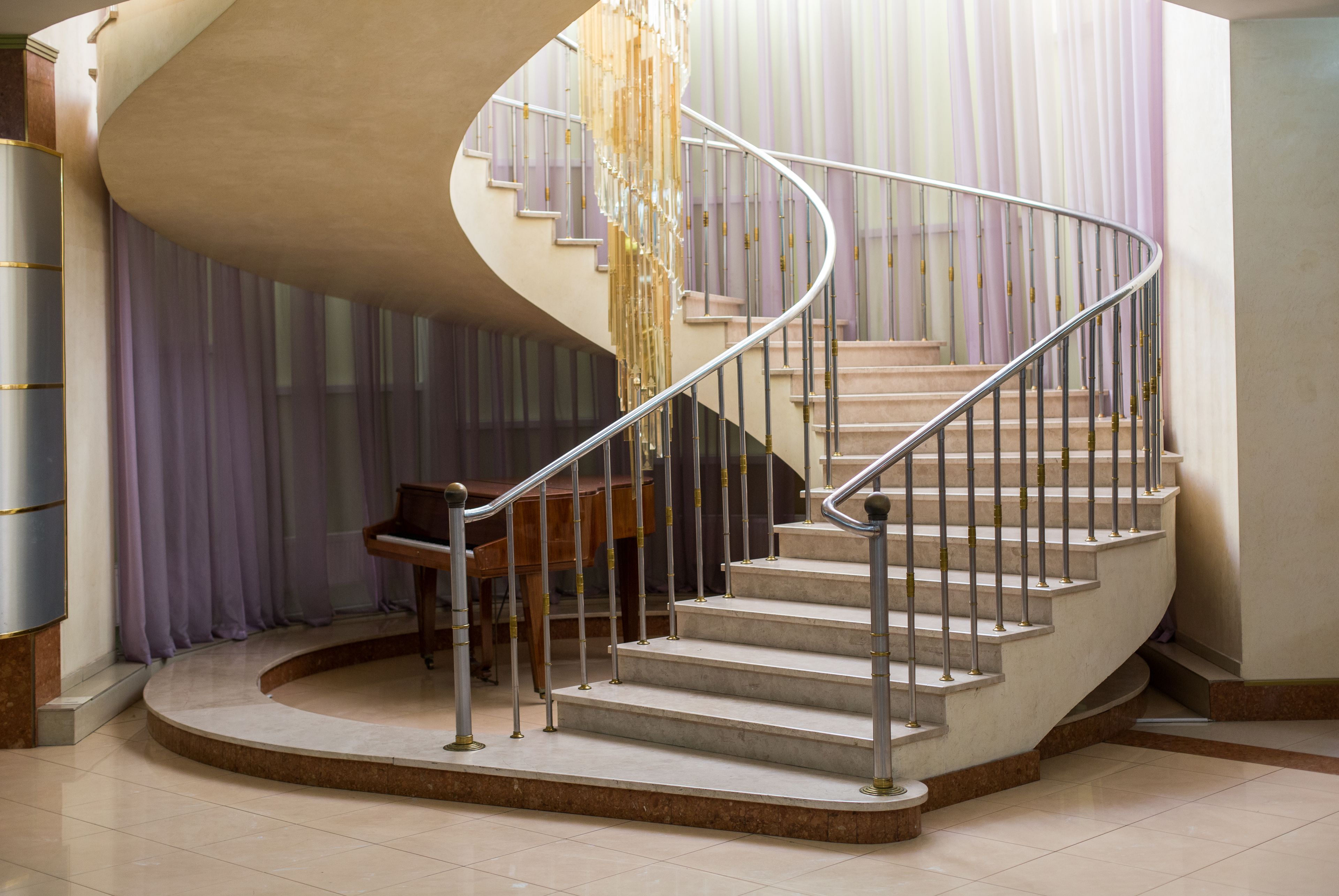A spiral staircase with a modern design, featuring a metal railing and a wooden piano near the bottom.