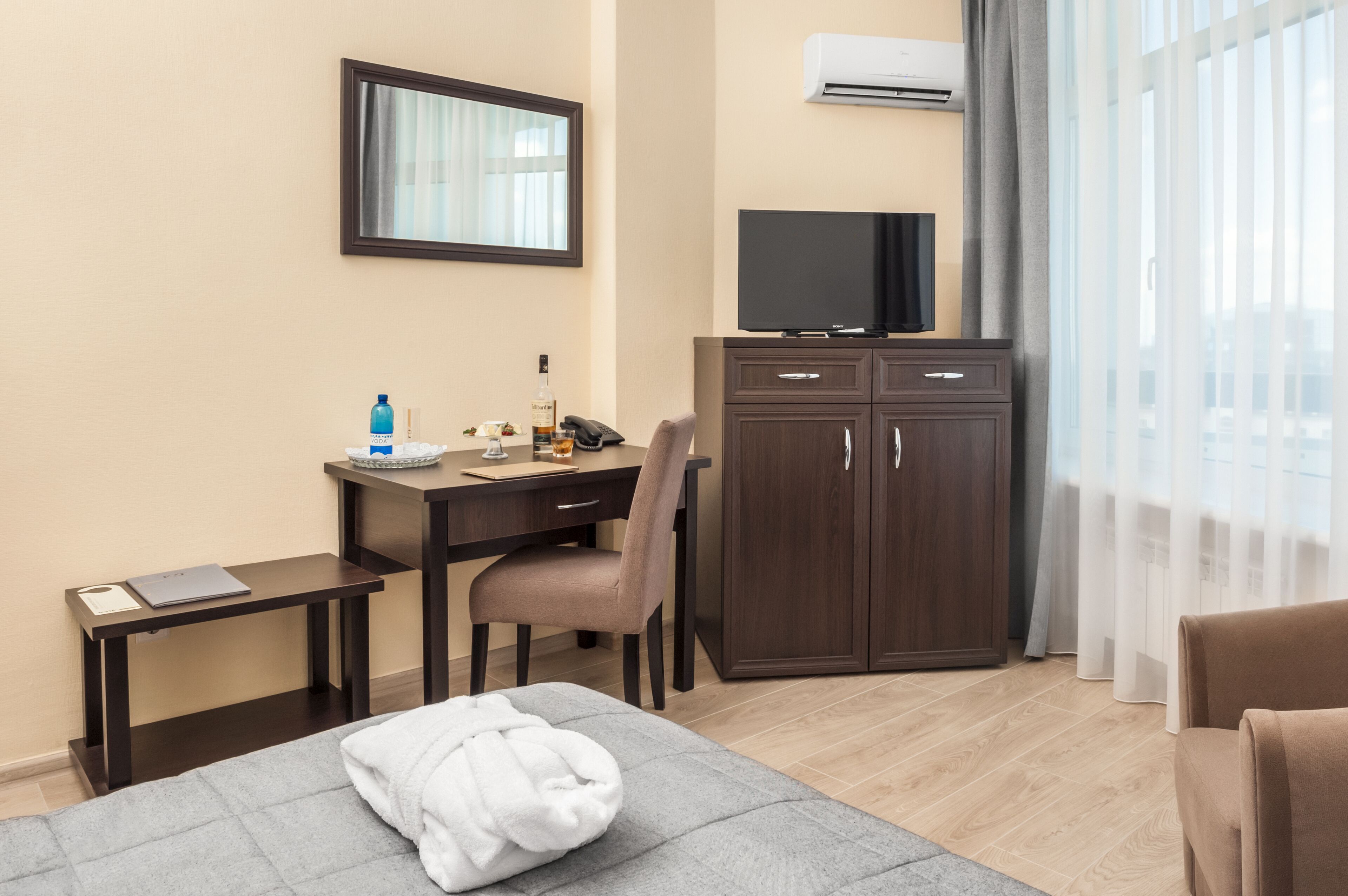 A hotel room with a bed, a desk with a chair, a TV on a cabinet, and a window with curtains.