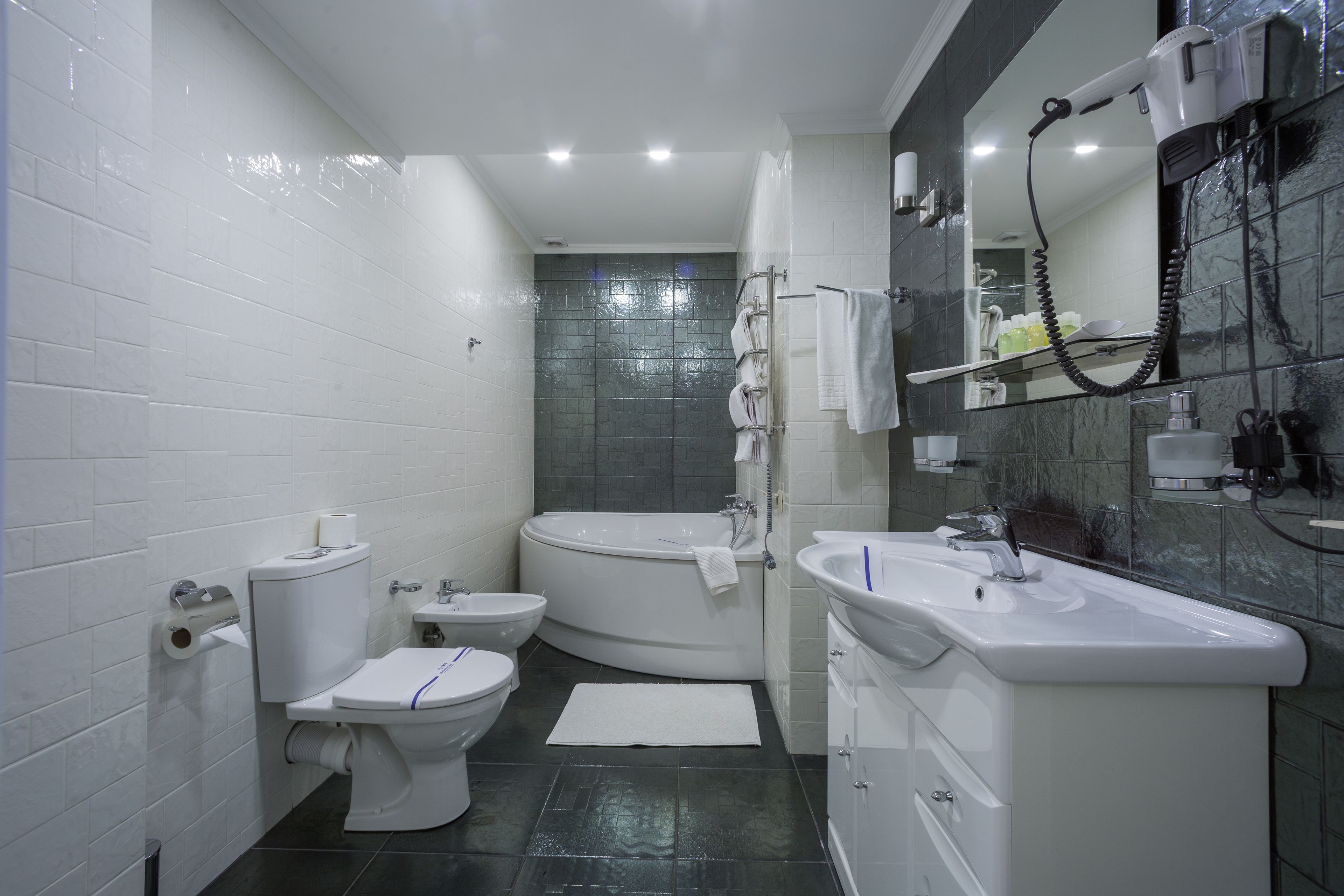 A modern bathroom with a toilet, bidet, bathtub, and a large mirror.