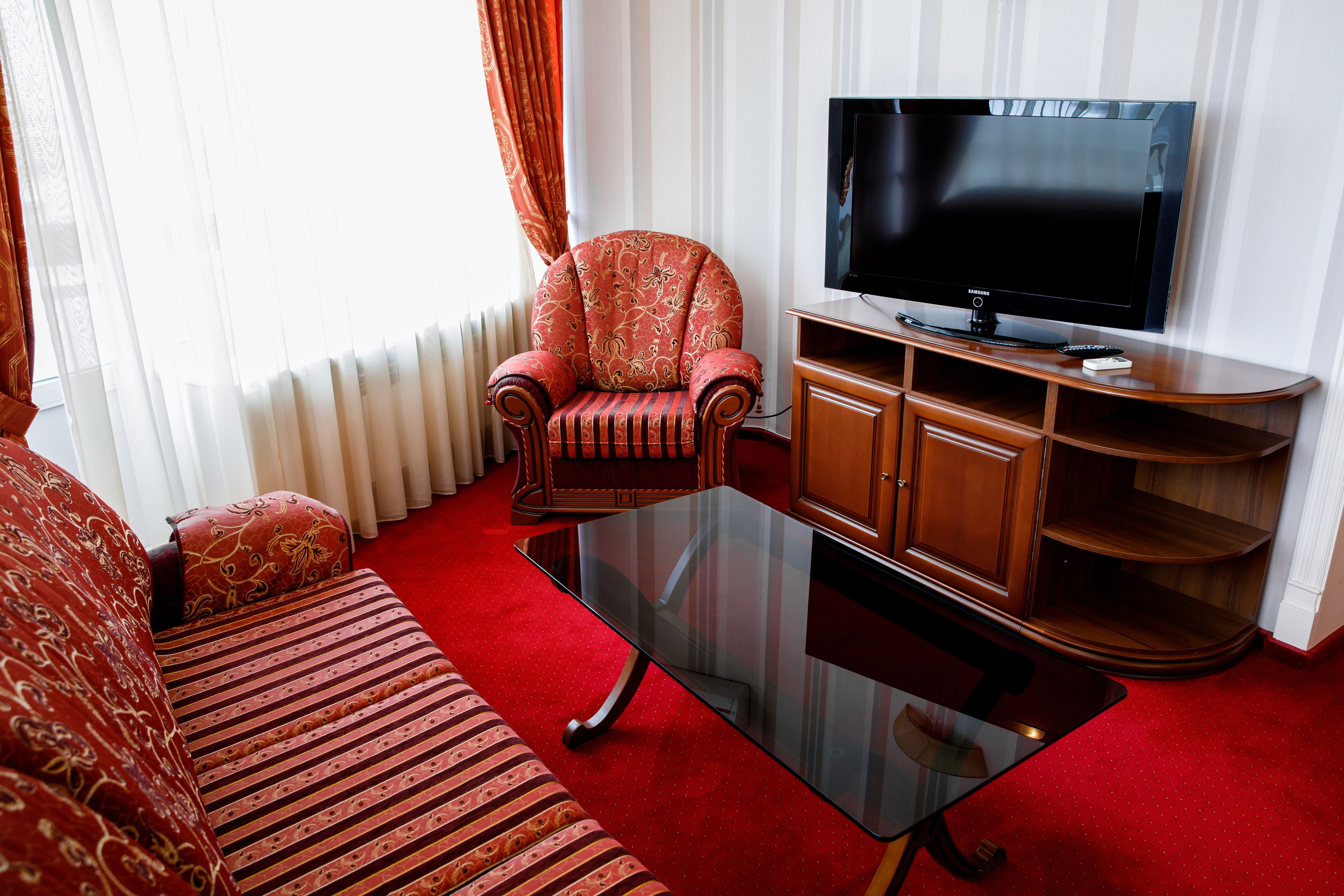 A living room with a sofa, armchair, glass coffee table, TV, and wooden entertainment unit.