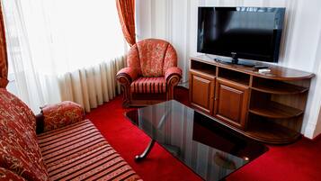 Ein Wohnzimmer mit Sofa, Sessel, Glastisch, Fernseher und einer Holz-Unterhaltungseinrichtung.