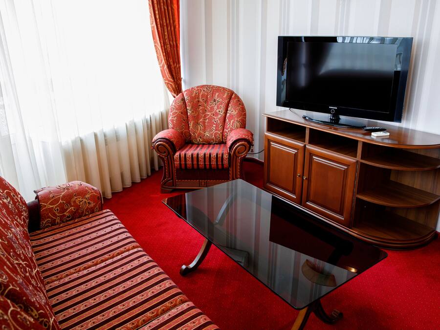Ein Wohnzimmer mit Sofa, Sessel, Glastisch, Fernseher und einer Holz-Unterhaltungseinrichtung.