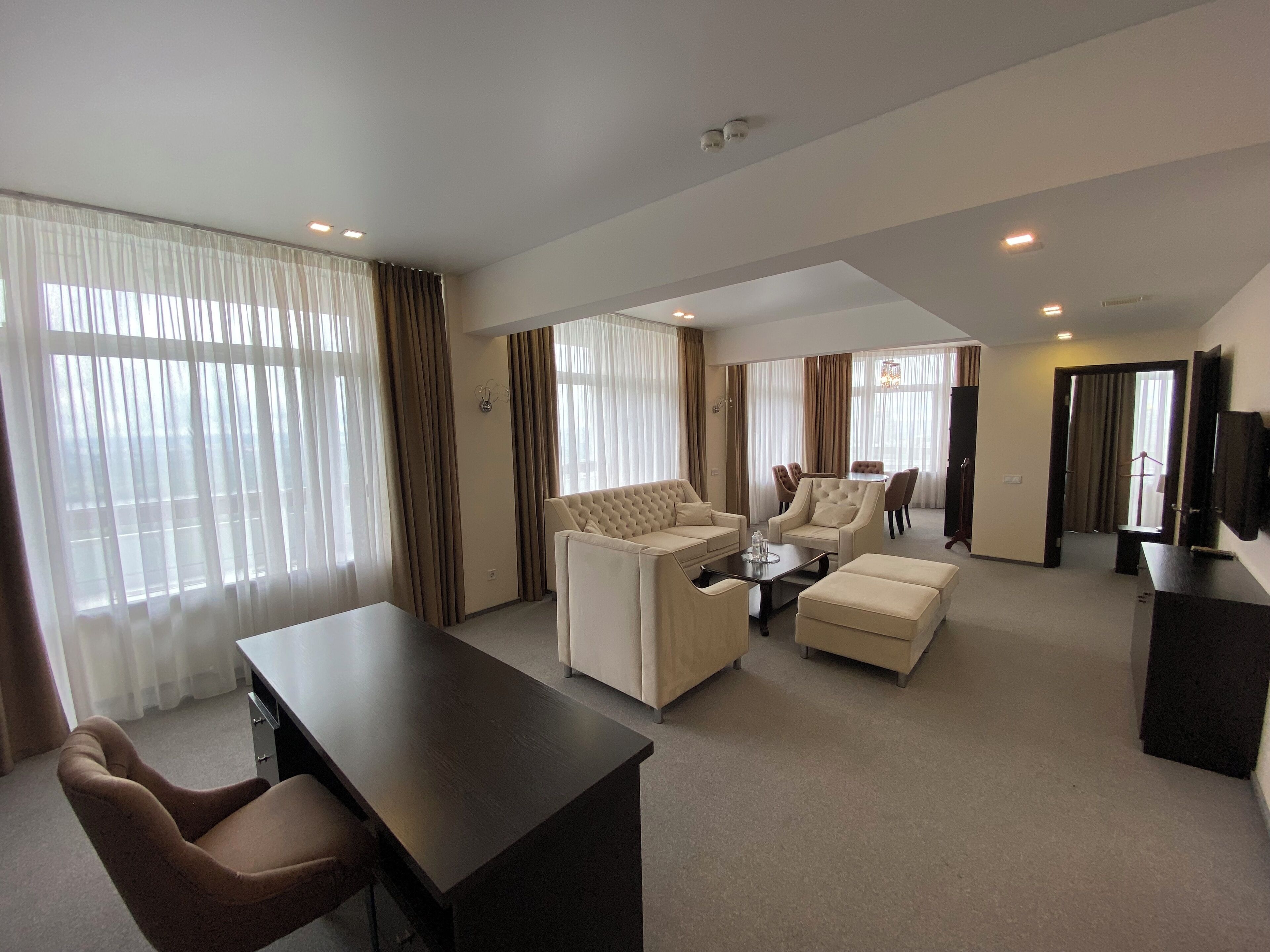A spacious hotel living room with a sofa set, a coffee table, and a TV on a stand.