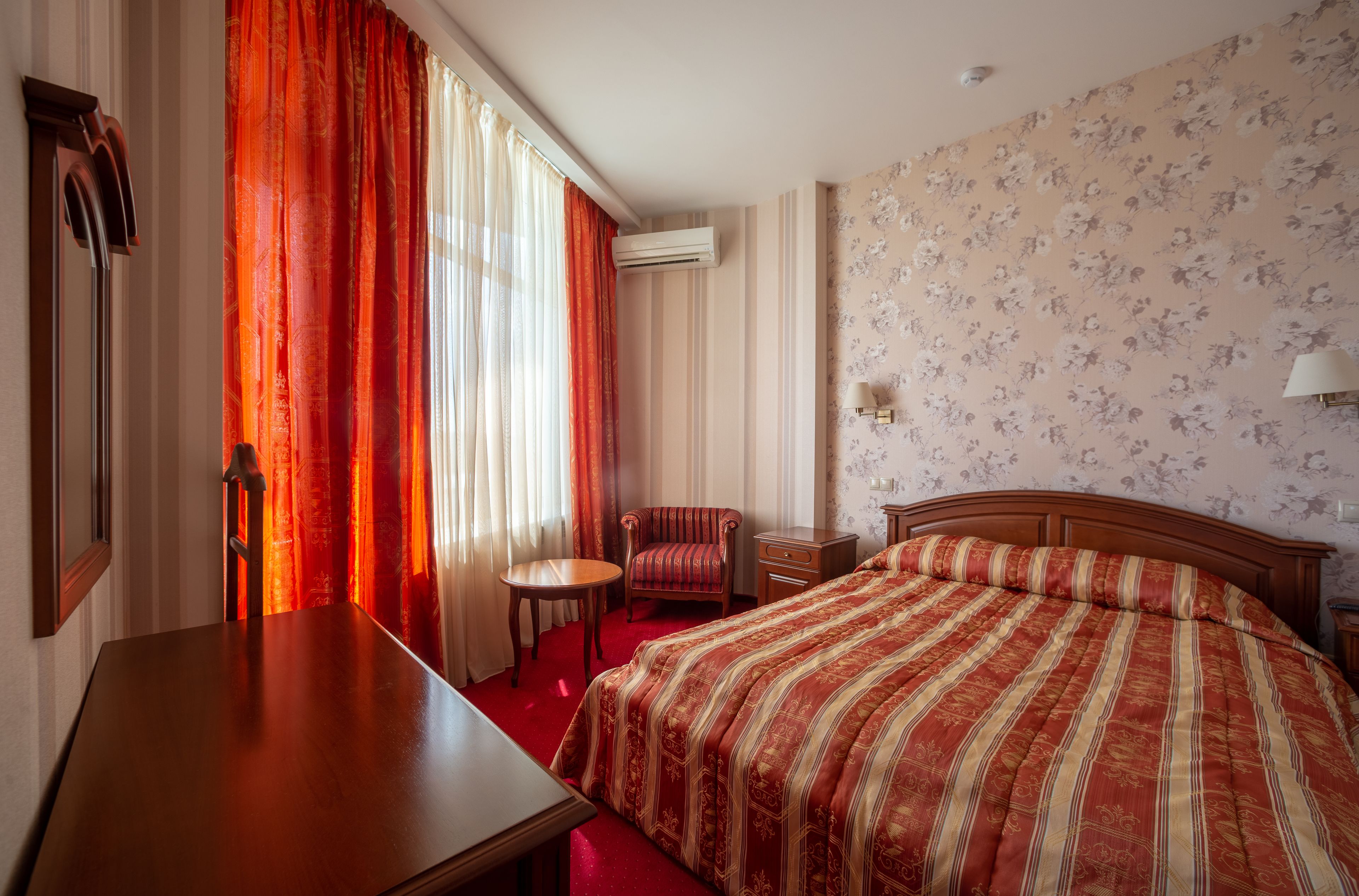 Une chambre d’hôtel avec un grand lit, un bureau en bois, une chaise, une petite table et une table de chevet.