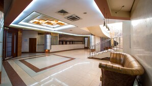 Eine geräumige Lobby mit hoher Decke, einer zentralen Sitzgruppe und einer Treppe zu den oberen Stockwerken.