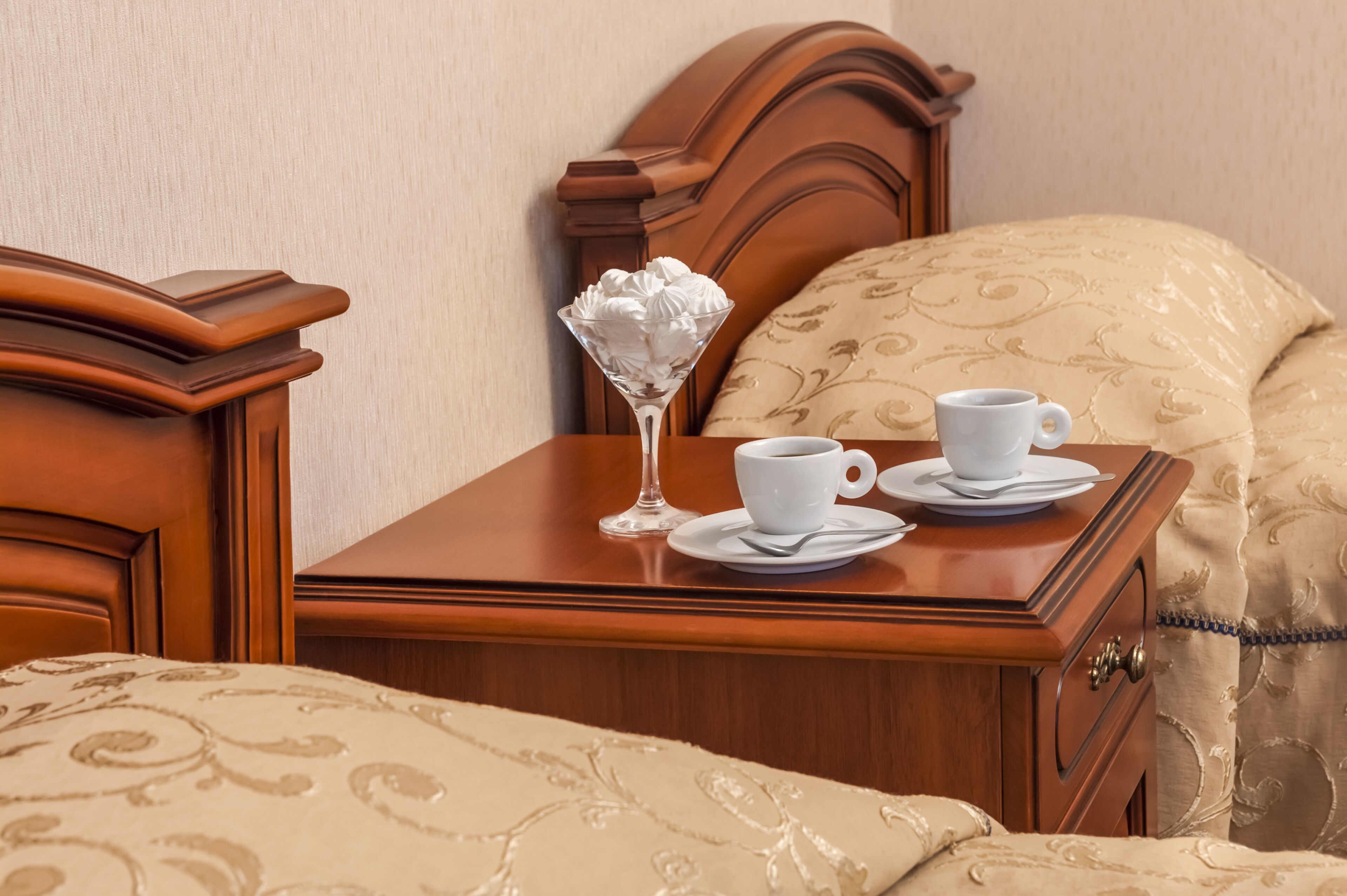 Una cama bien hecha con una colcha estampada, una mesita de noche con una taza de café y un vaso decorativo, y un cabecero de madera.
