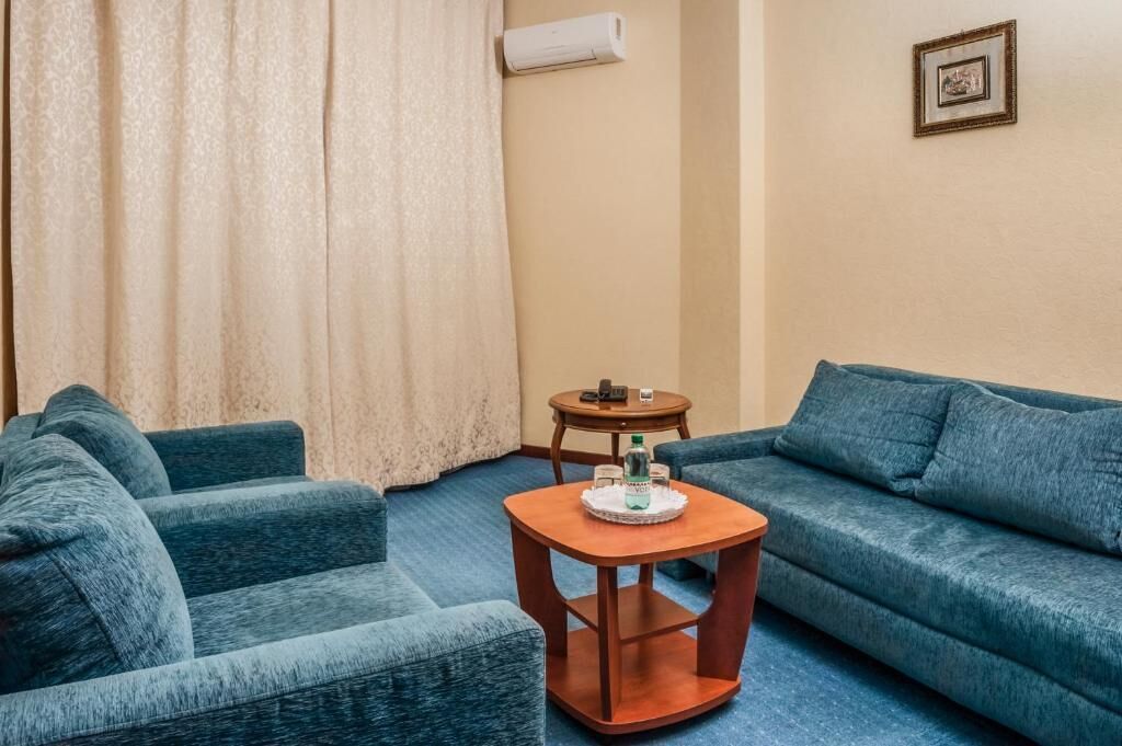 Una sala de estar con un sofá azul, una mesa de centro de madera con una bandeja y una mesita con un teléfono y una botella.