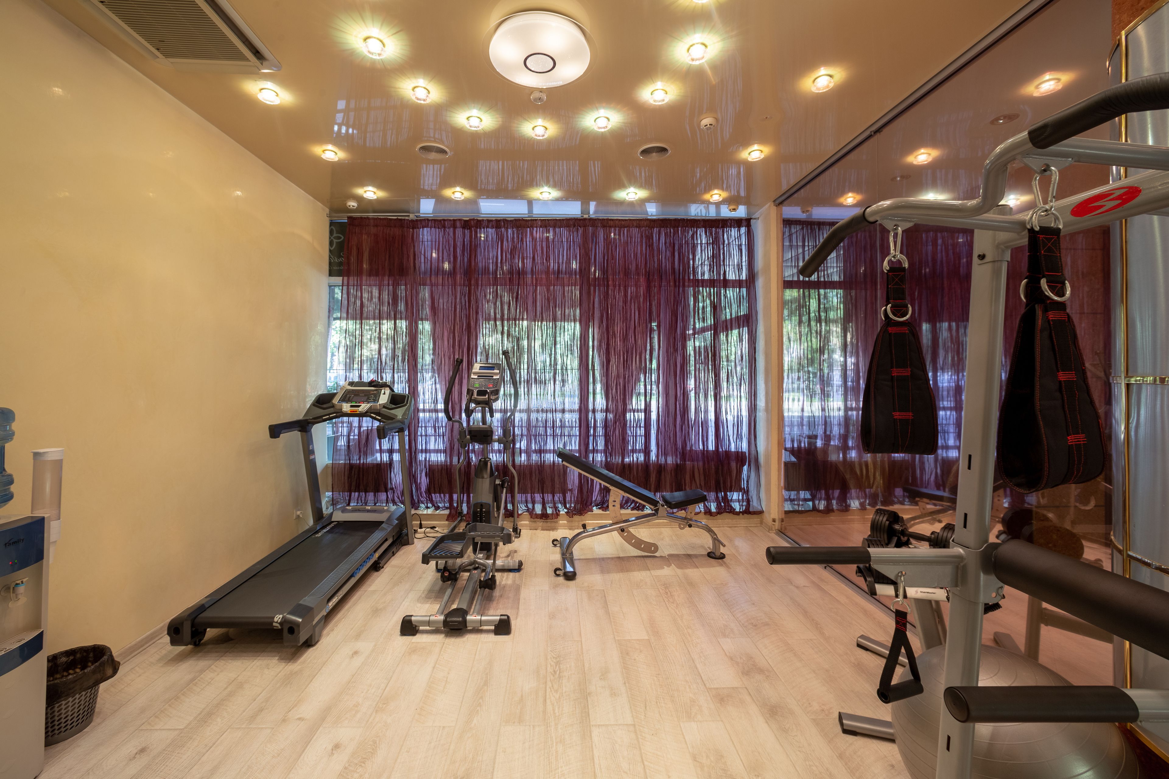 Een sportschool met loopband, elliptische trainer, bankdrukrek en diverse gewichten.