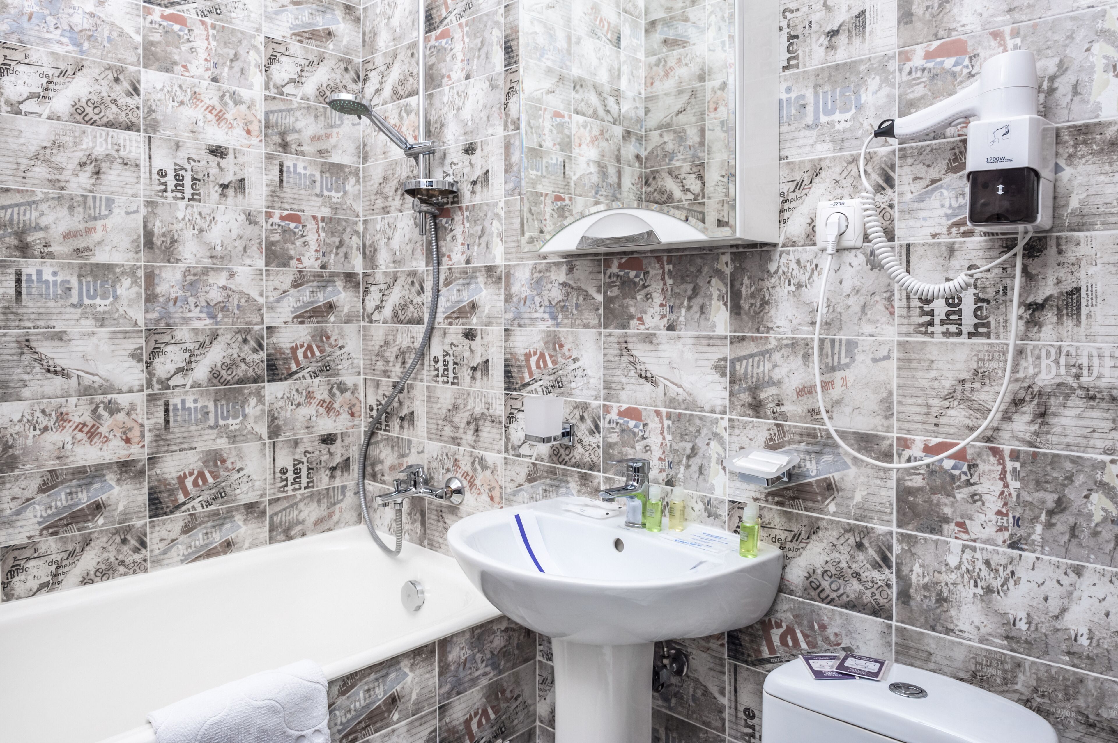 A bathroom with a shower, a sink, and a hairdryer mounted on the wall.