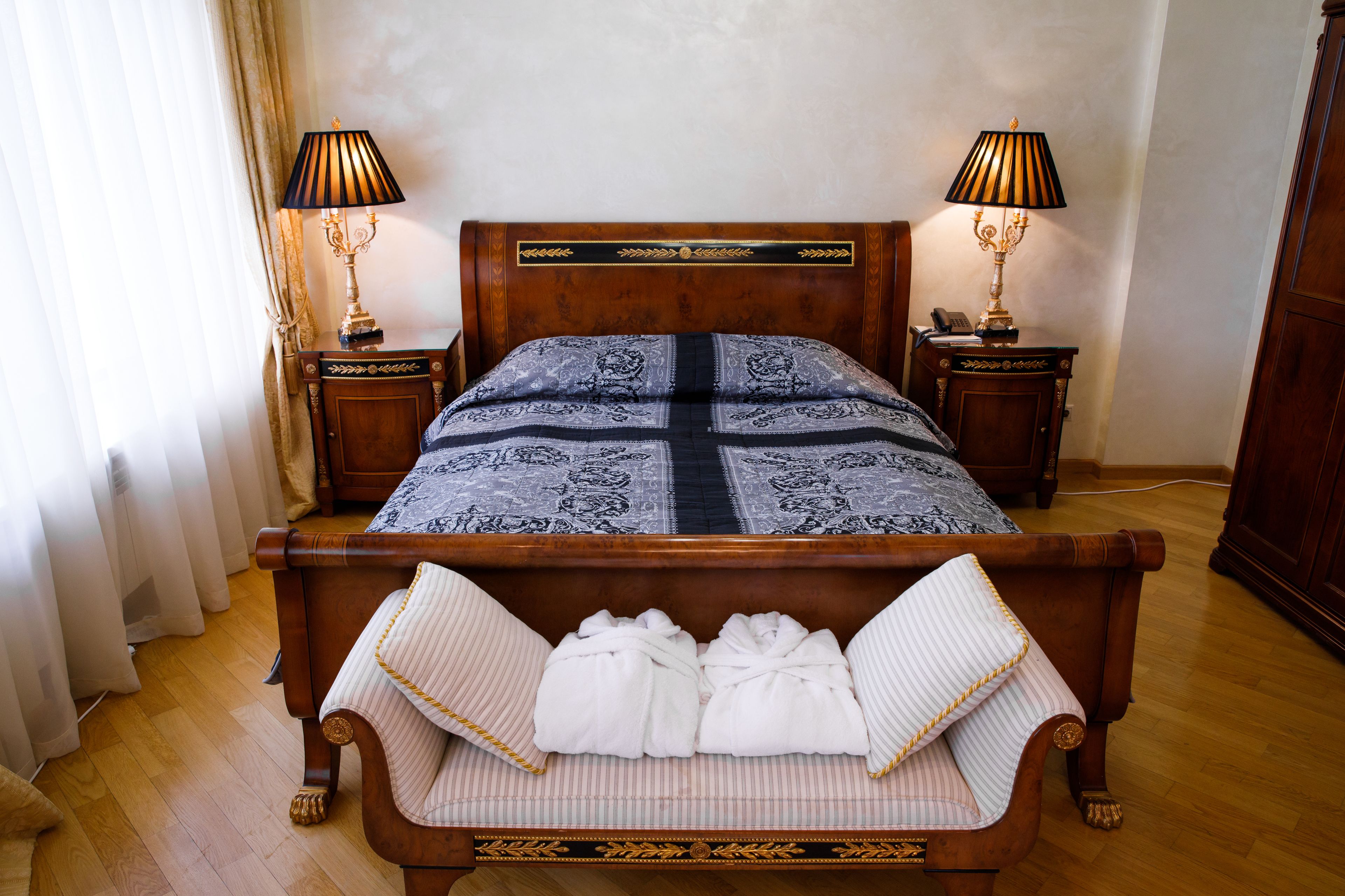 Un lit bien fait, recouvert d’une couvre-lit à motifs, deux tables de chevet avec des lampes et une paire de serviettes posées sur un banc.