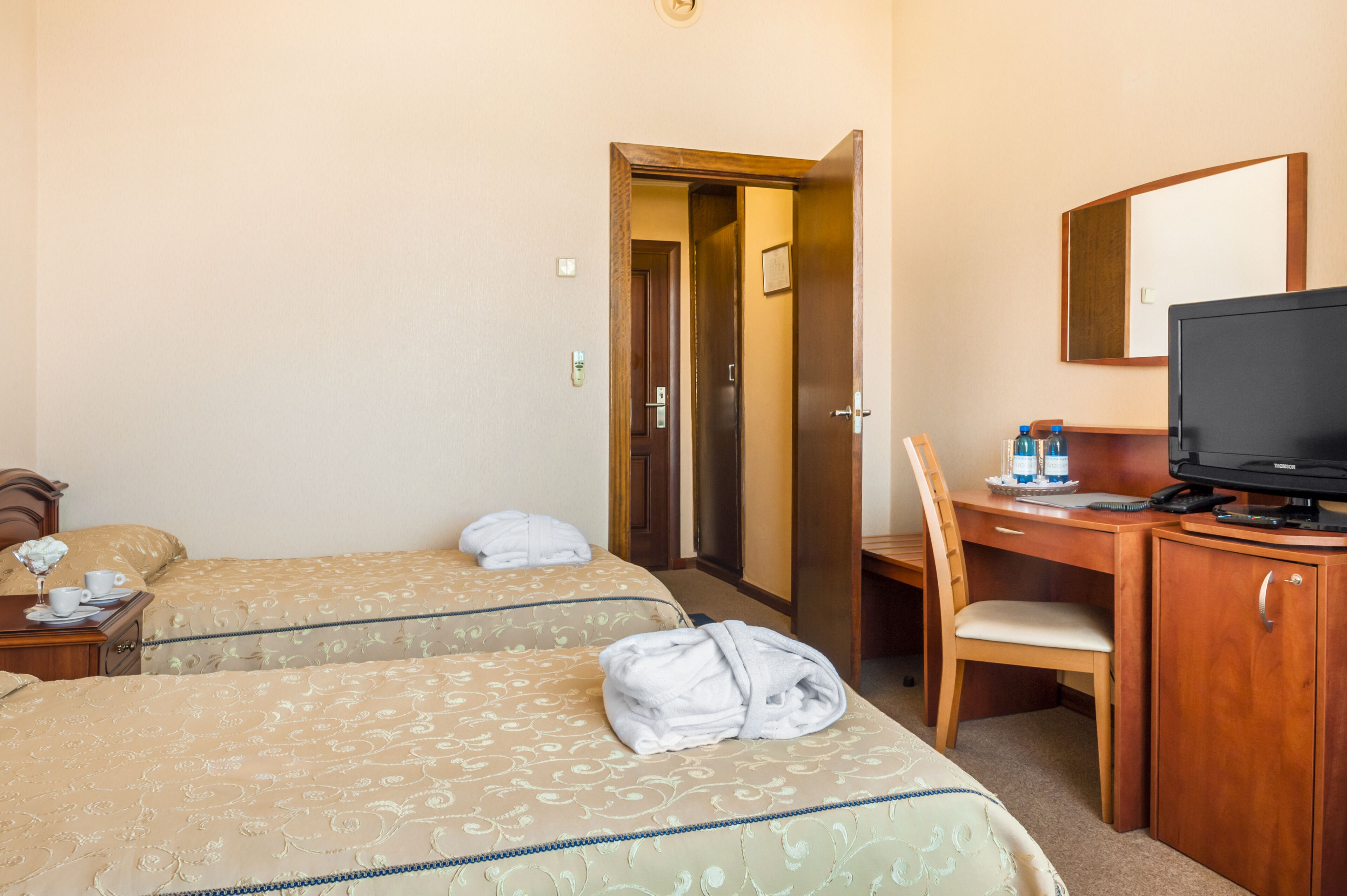 Habitación de hotel con dos camas, un escritorio con silla, televisor y puerta de baño.