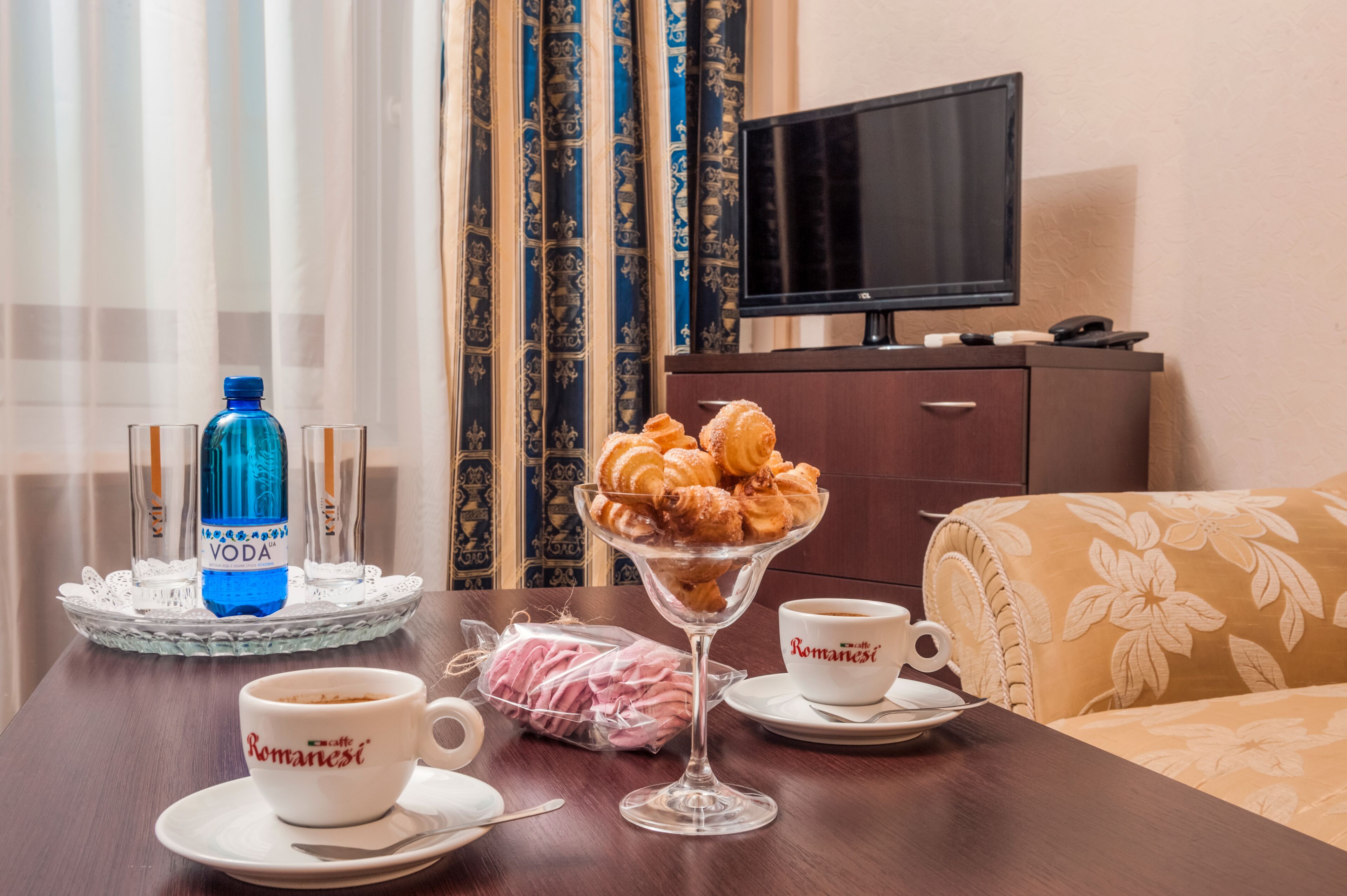 A hotel room with a dining table set for breakfast, including croissants, a glass of water, and a cup of coffee.