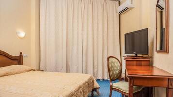 A hotel room with a bed, a desk with a chair, a television, and a large window with curtains.