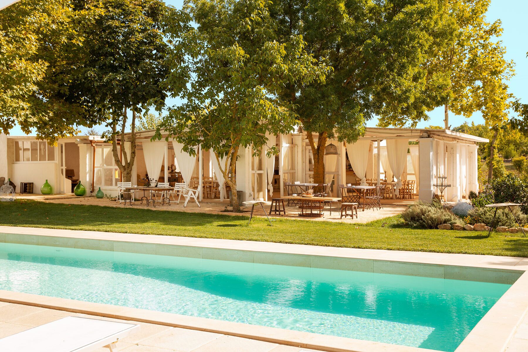 Una zona junto a la piscina con mobiliario exterior y un porche cubierto.