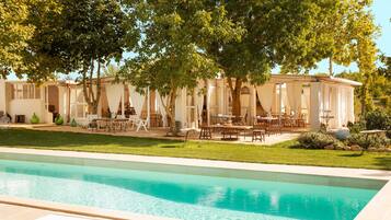 Una zona junto a la piscina con mobiliario exterior y un porche cubierto.