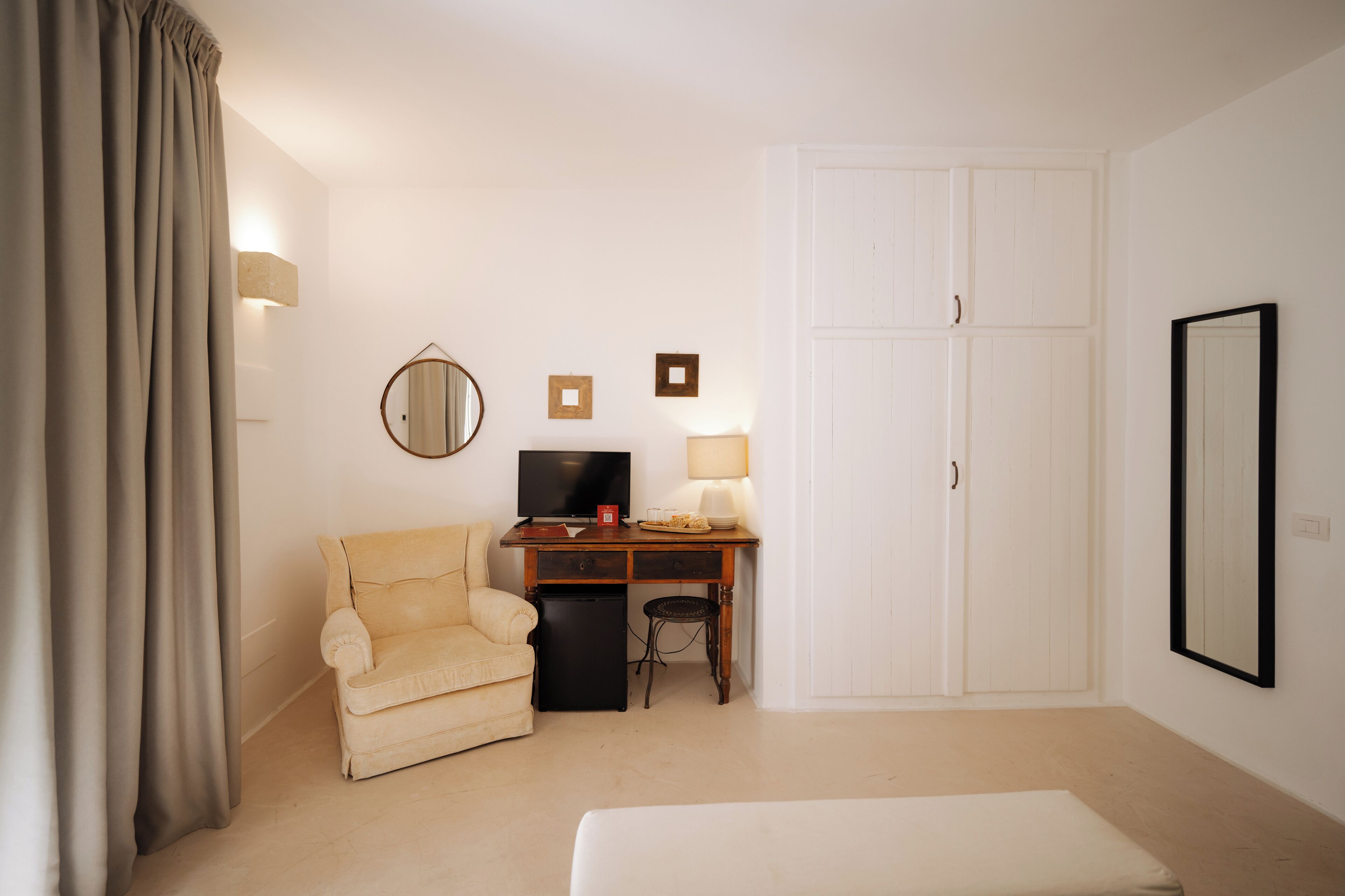 Habitación de hotel con cama, escritorio con televisor, silla, mesa pequeña y armario.