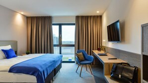 Et hotelværelse med seng, skrivebord, stol, fjernsyn og udsigt til det fri.