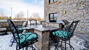 Un patio al aire libre con un muro de piedra, una parrilla y sillas de metal con cojines.