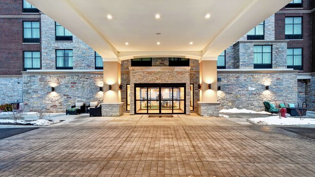 Una entrada de hotel con fachada de piedra, puerta de cristal y zona pavimentada con ladrillos.