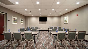 Une salle de conférence dotée d’un sol recouvert de moquette, de plusieurs tables, de chaises et d’un téléviseur à écran plat fixé au mur.