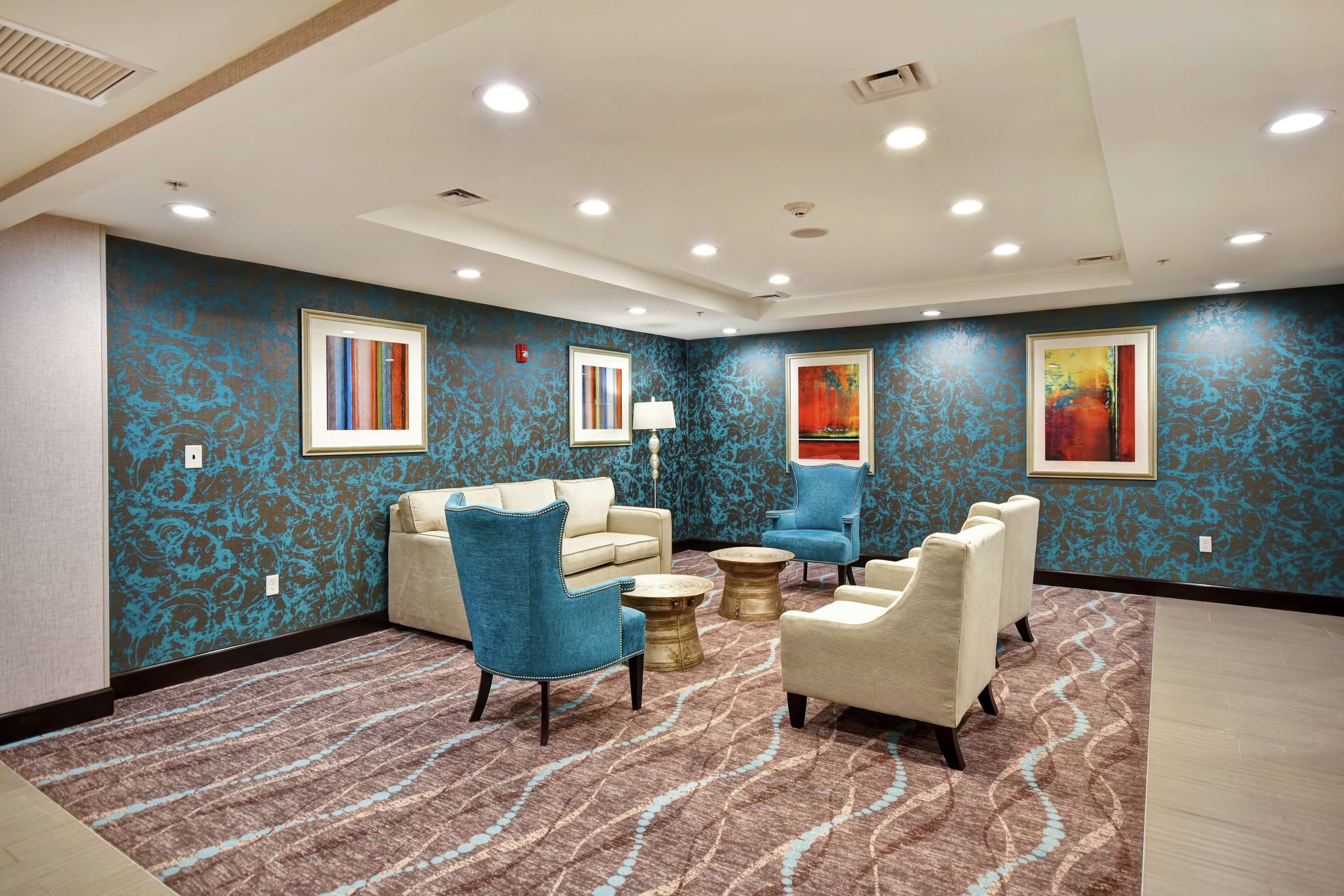 A hotel room with a patterned carpet, a beige sofa, a blue armchair, and a small round table.